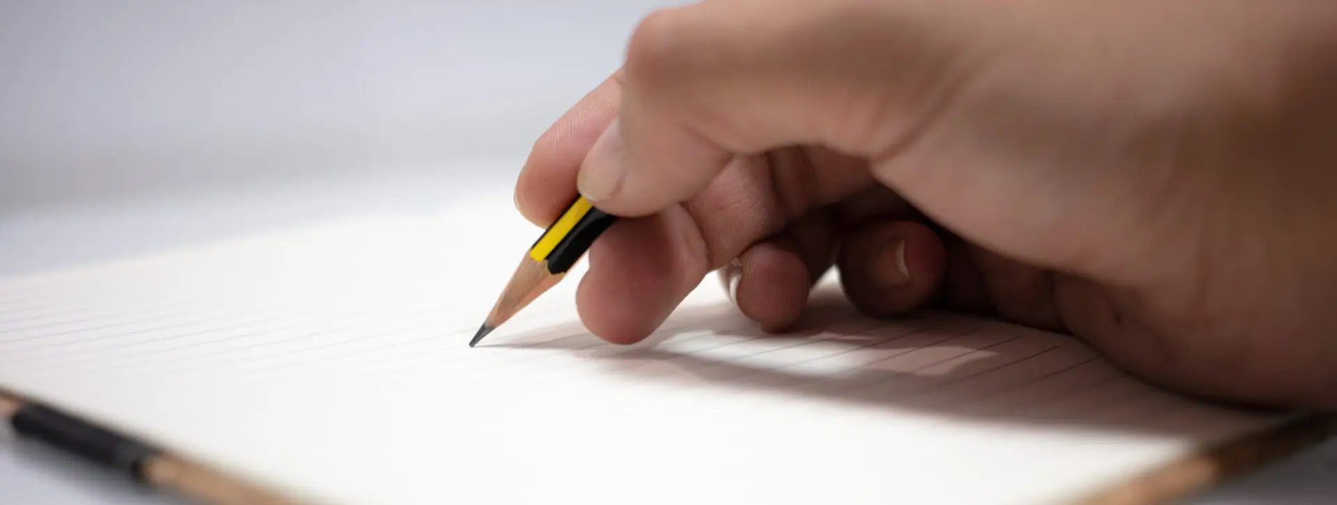 Hand, die mit einem Bleistift auf ein liniertes Blatt schreibt